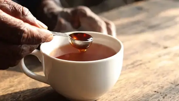 A thick dark syrup sliding off a quarter-teaspoon measure into a cup of tea