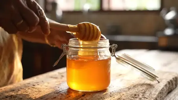 A thick ribbon of golden honey falling slowly from a wooden dipper into an open jar